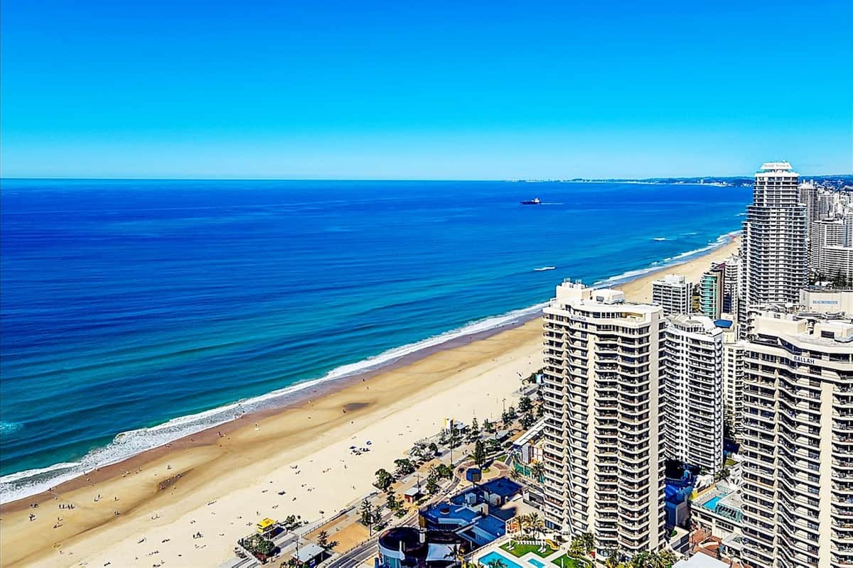 Een hoog hotel met uitzicht op het strand, meerdere balkons en een zwembad.