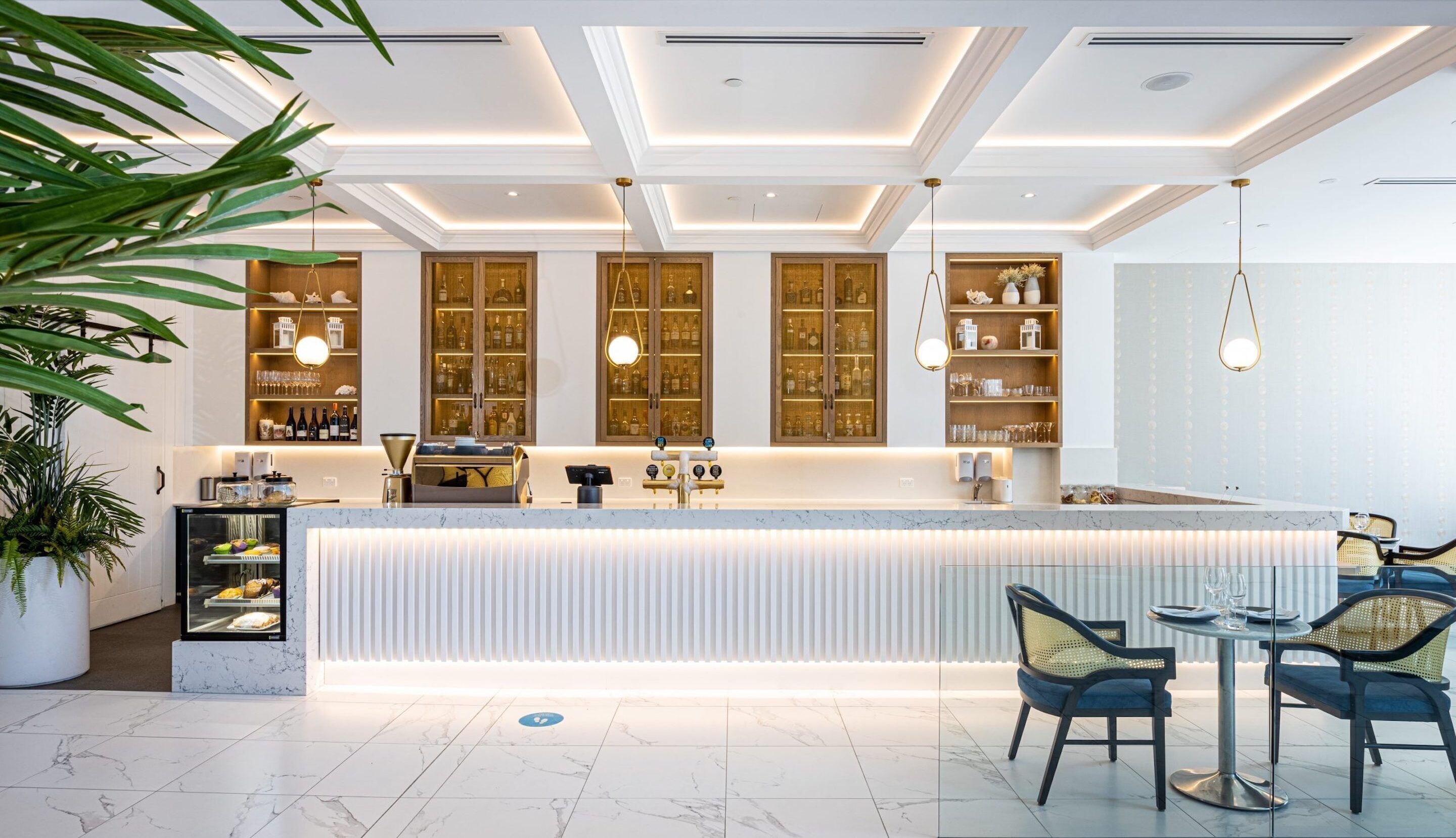 Un espace bar moderne doté d’un comptoir en marbre, de meubles en bois et de luminaires suspendus.