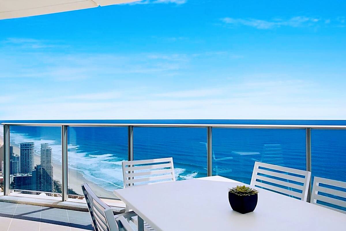 Een balkon met een witte tafel en stoelen, met uitzicht op een stad en de oceaan.