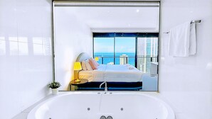 A modern bathroom with a large bathtub, a glass-enclosed shower, and a view of a bedroom with a bed and a cityscape. - Circle On Cavill Surfers Paradise Apartments-Holiday Paradise (Surfers Paradise)