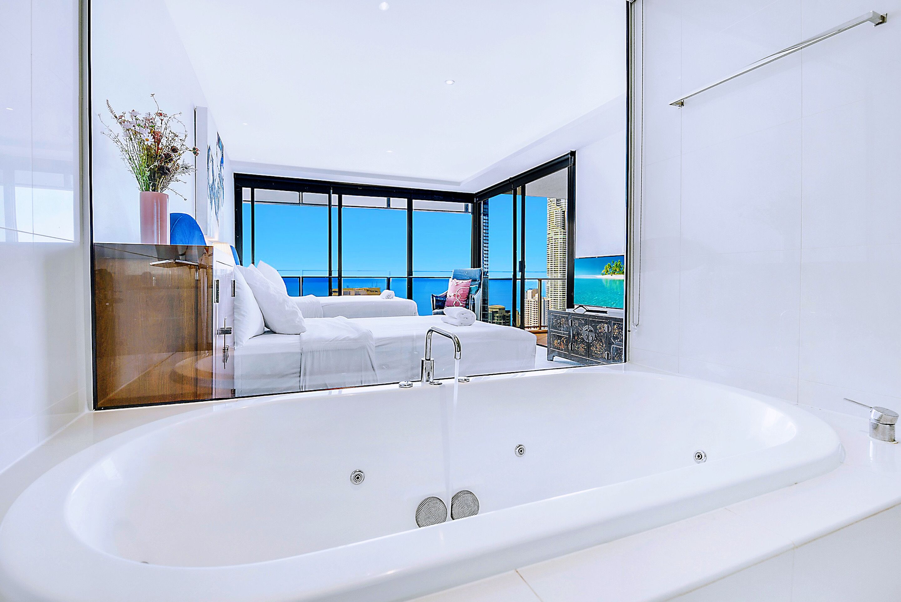 A modern bathroom with a large white bathtub, a glass-enclosed shower area, and a view of the sea through large windows.