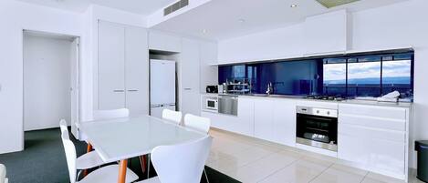 A modern kitchen with white cabinetry, a large island with a built-in oven, and a view of the city through large windows.