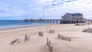 Una playa con un muelle de madera que lleva a una casa grande con varias ventanas y un balcón.