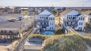 Zona residencial costera con casas de varios pisos, una piscina y una playa en primer plano.