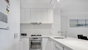 A modern kitchen with white cabinetry, a built-in oven, a dishwasher, and a stainless steel range hood. - MJ Shortstay Whiteman St Apartments (Southbank)