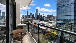A balcony with a view of a city skyline, a table, and a chair. - MJ Shortstay Whiteman St Apartments (Southbank)