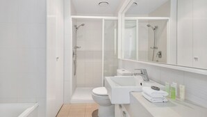 A modern bathroom with a glass-enclosed shower, a toilet, and a sink with a mirror above. - MJ Shortstay Whiteman St Apartments (Southbank)