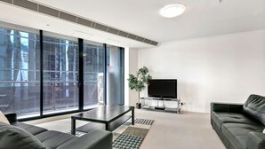 A modern living room with a large window, a flat-screen TV, a coffee table, and a sofa. - MJ Shortstay Whiteman St Apartments (Southbank)