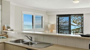 A modern kitchen with a double sink, a window with blinds, a lamp, and a view of the outdoors.
