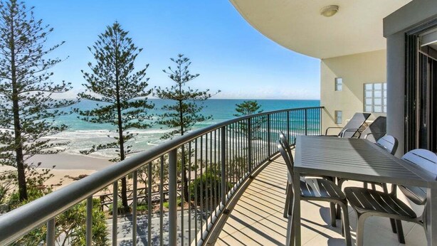 A balcony with a view of the beach and ocean, a table with chairs, and a railing.