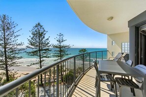 A balcony with a view of the beach and ocean, a table with chairs, and a railing.