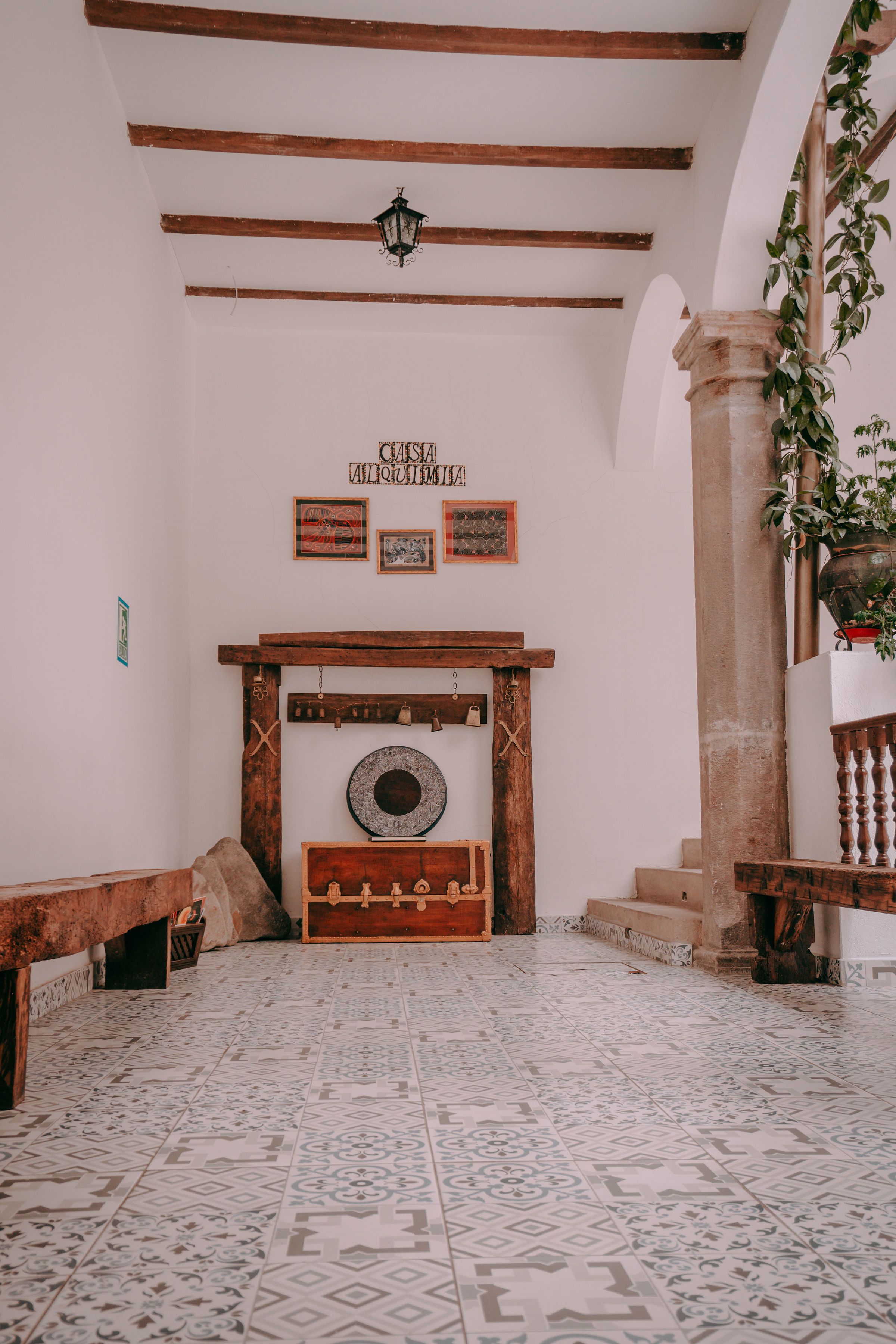 A room with a fireplace, wooden beams, patterned floor tiles, and a stone column.