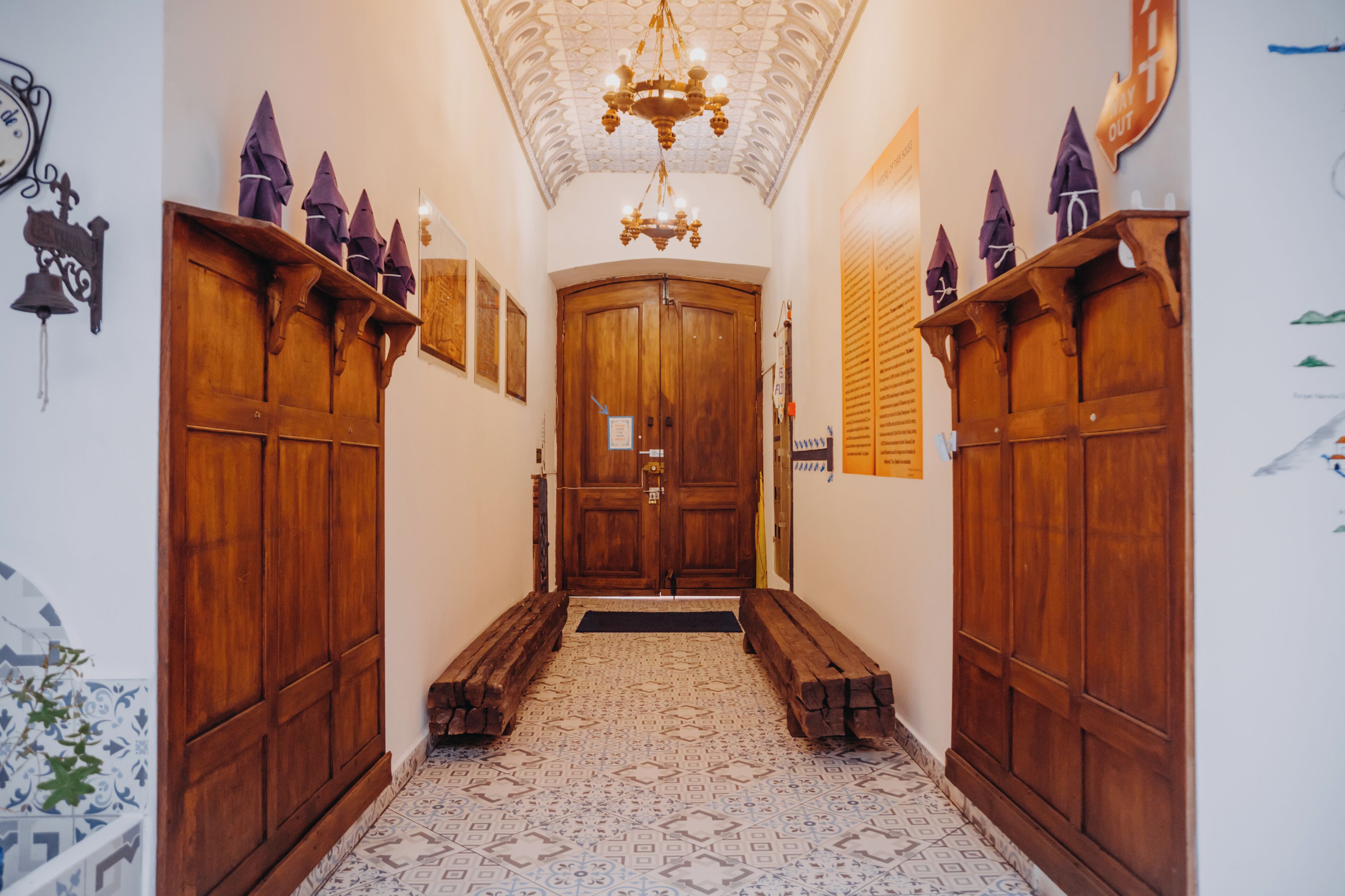 A hallway with wooden doors, a chandelier, and patterned floor tiles.