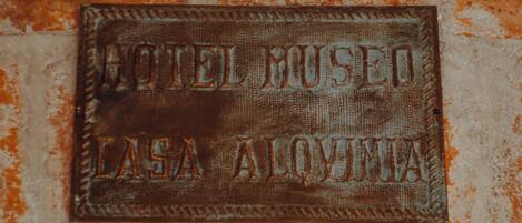 A weathered metal sign with the text "HOTEL MUSEO LASA ALQUMA" on a brick wall.