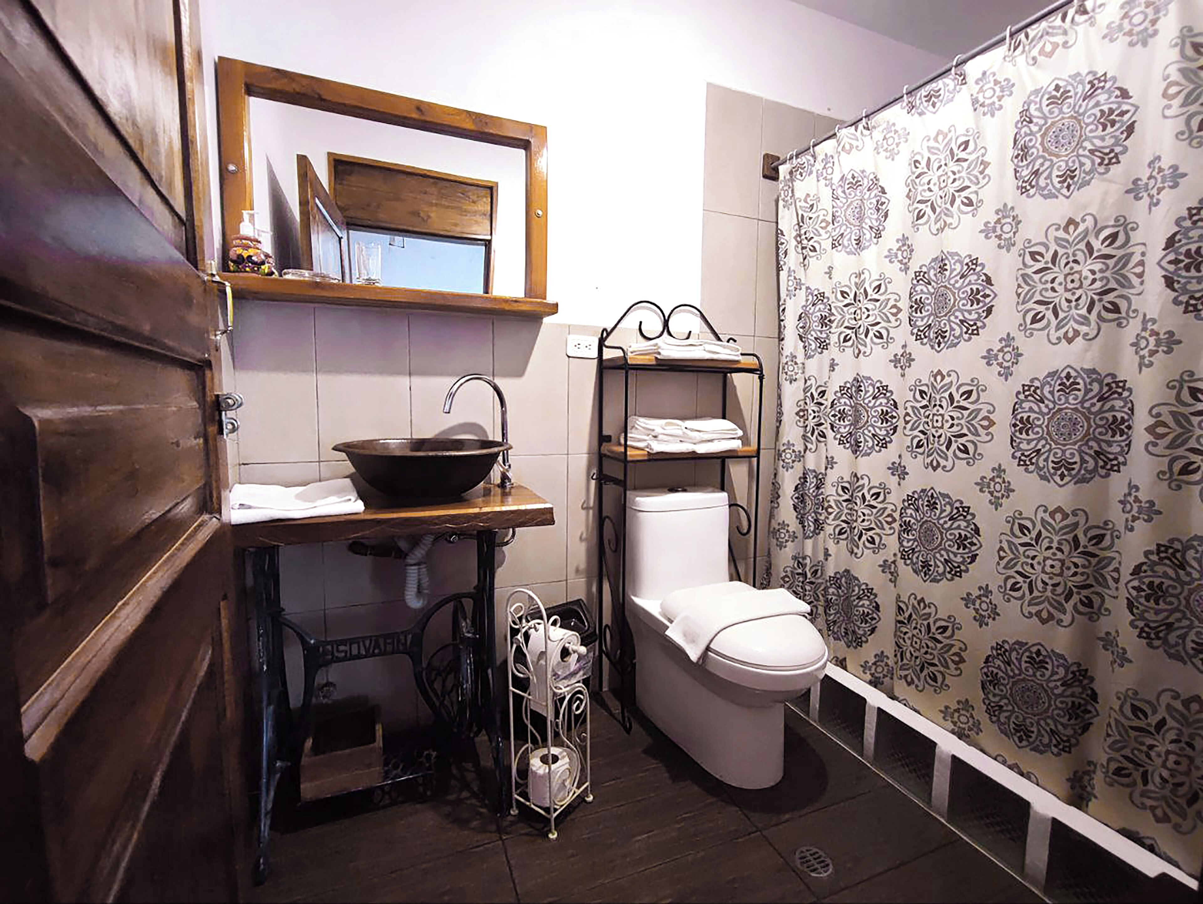 A compact bathroom with a wooden vanity, a vessel sink, a toilet, and a shower curtain with a floral pattern.