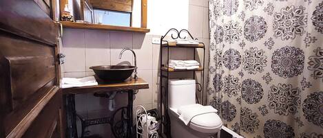 A compact bathroom with a wooden vanity, a vessel sink, a toilet, and a shower curtain with a floral pattern.