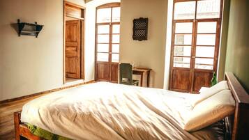 A bedroom with a bed, wooden wardrobe, arched windows, and a small desk.