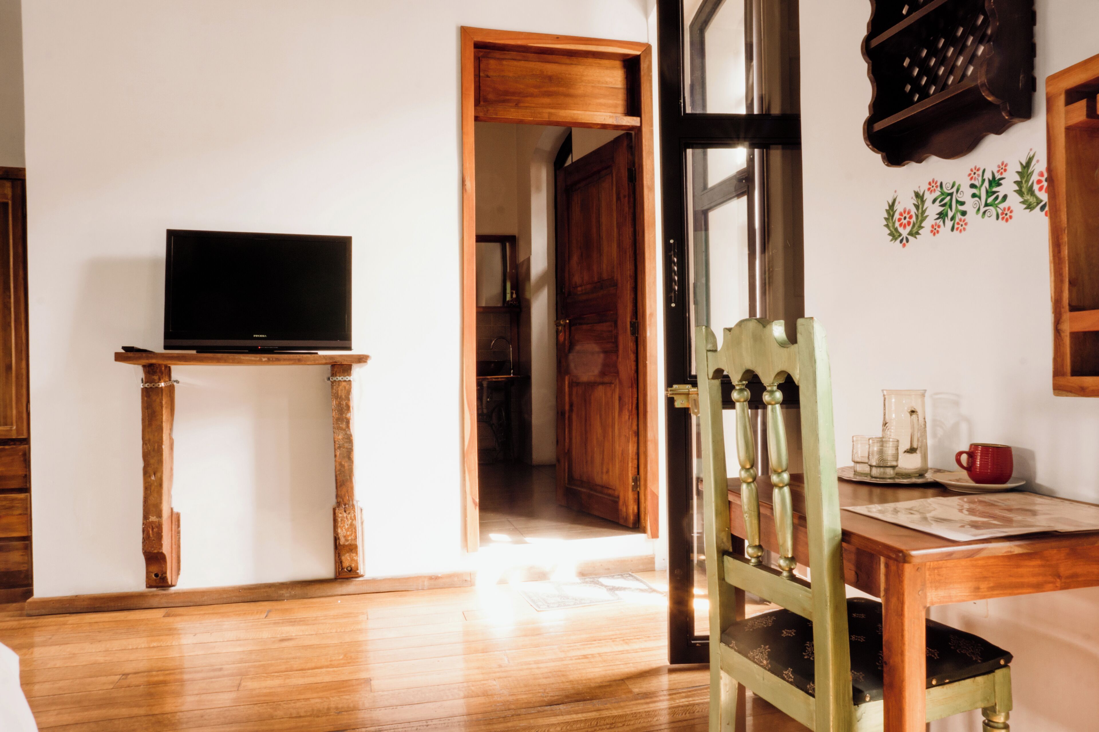 A room with a wooden floor, a television on a stand, a wooden door, and a chair with a cushion.