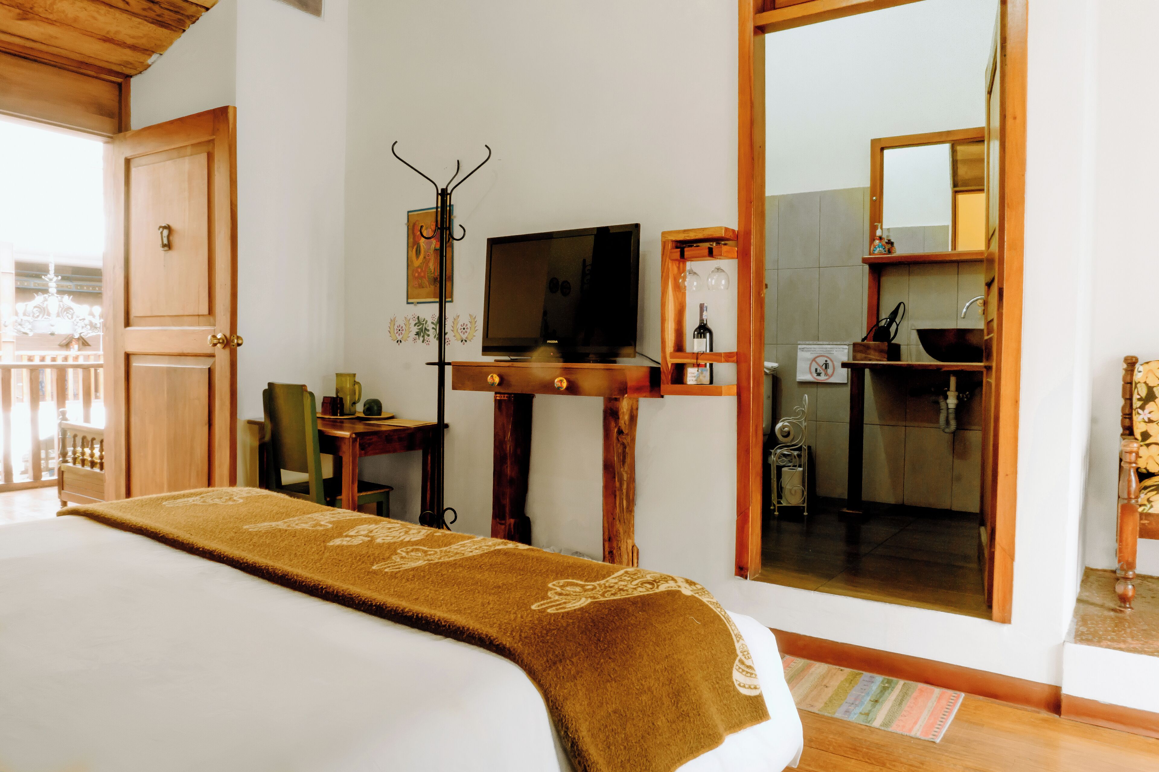 A hotel room with a bed, a television, a wooden desk, a mirror, and a view of the bathroom.