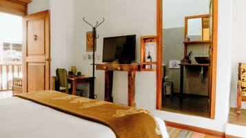 A hotel room with a bed, a television, a wooden desk, a mirror, and a view of the bathroom.