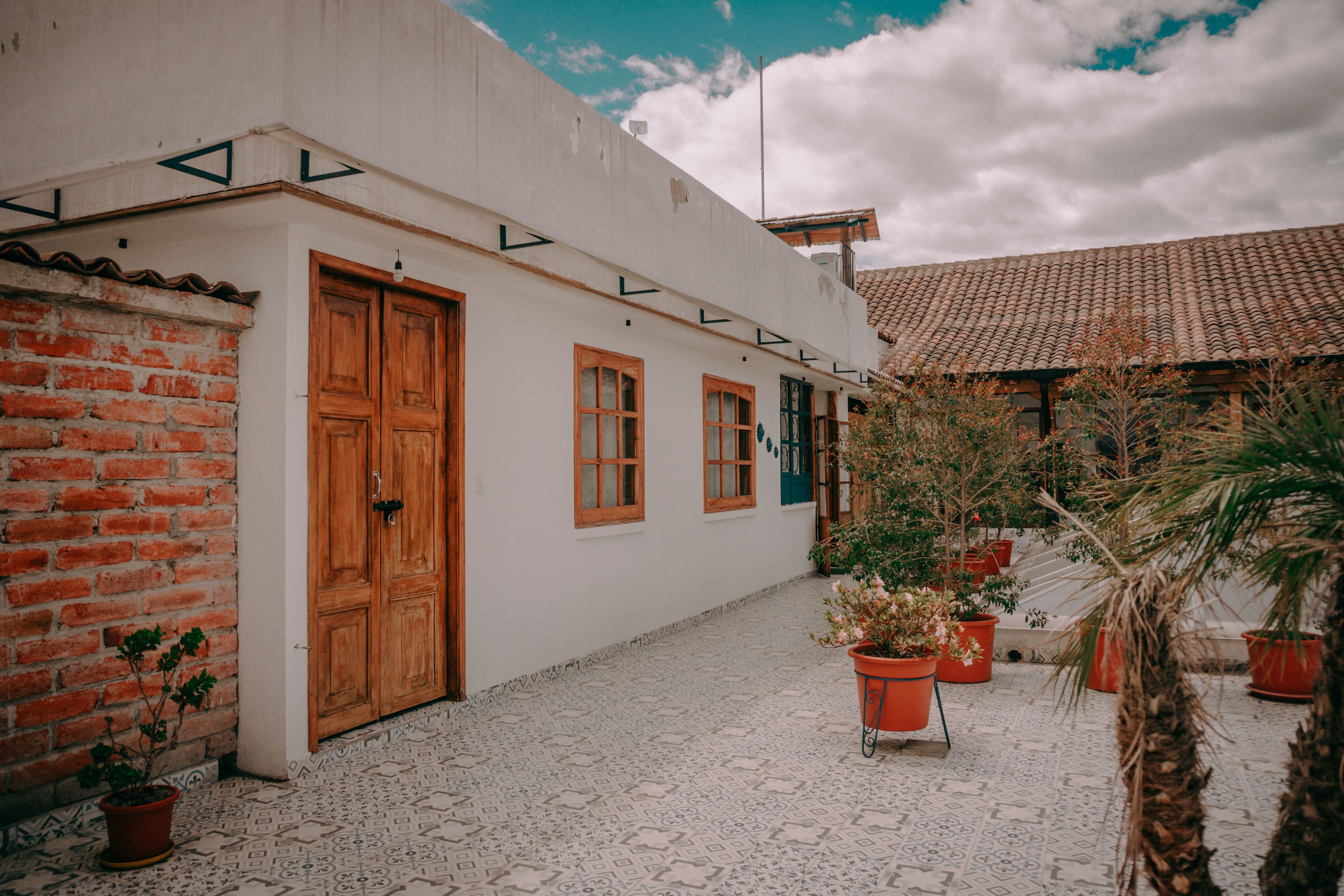 A courtyard with a white building, wooden doors, and potted plants.