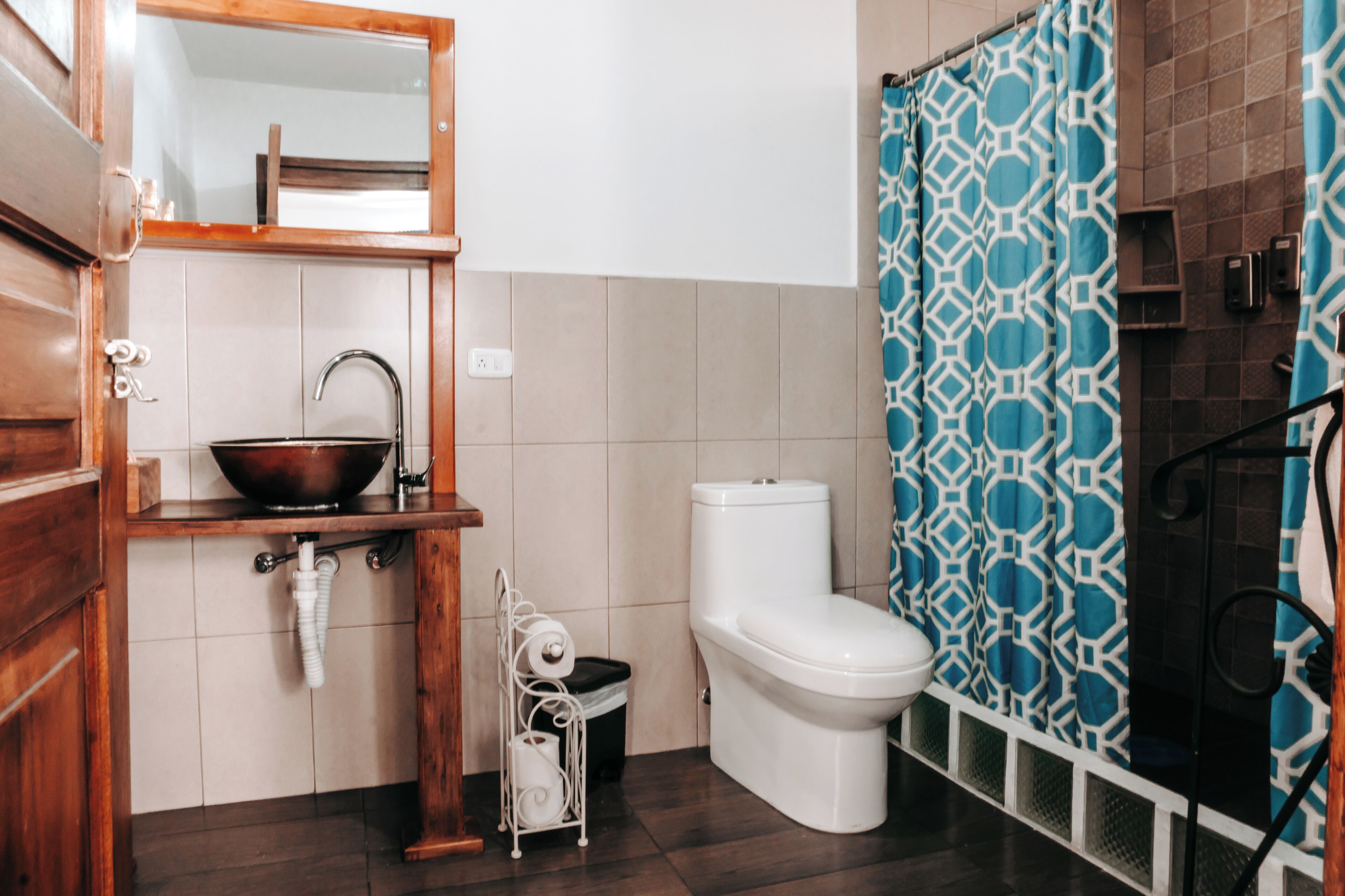 A bathroom with a wooden vanity, a white sink, a white toilet, and a blue patterned shower curtain.