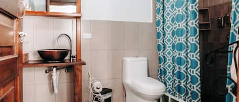 A bathroom with a wooden vanity, a white sink, a white toilet, and a blue patterned shower curtain.