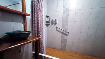 A bathroom with a wooden vanity, a large basin, a shower with a metal grab bar, and a patterned shower curtain.