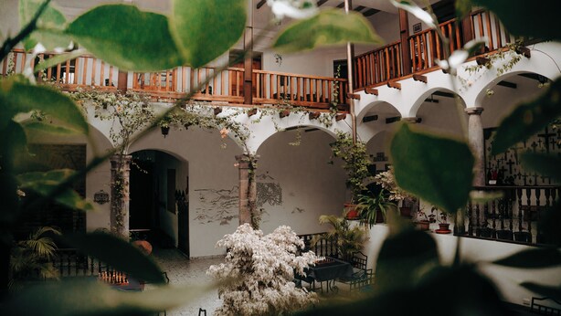 An indoor courtyard with arches, a wooden staircase, and potted plants. - Hotel Casa Alquimia (Quito)