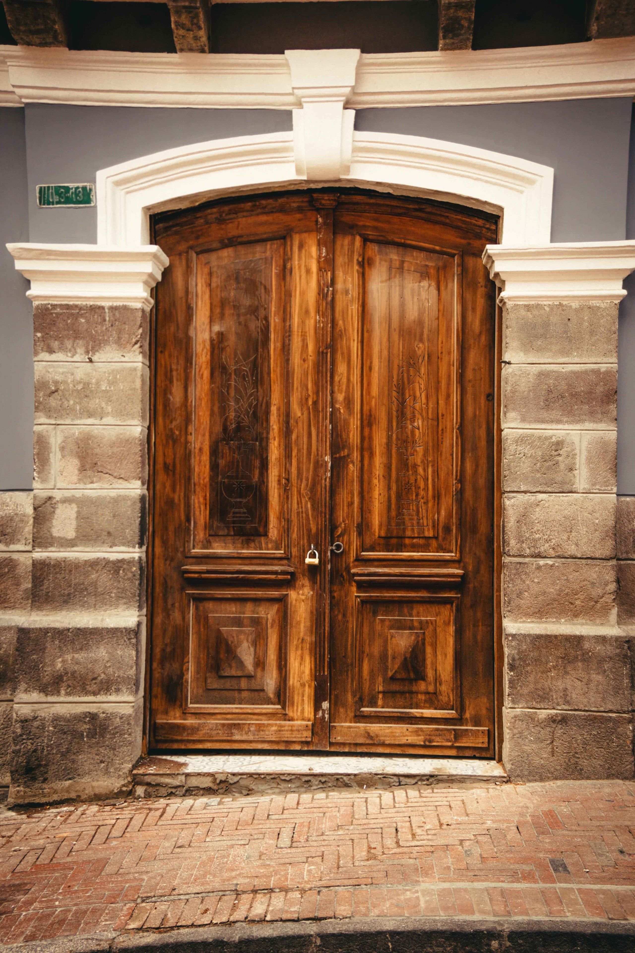 Unas amplias puertas de madera dobles con diseño tradicional, integradas en una pared de ladrillo con molduras blancas.