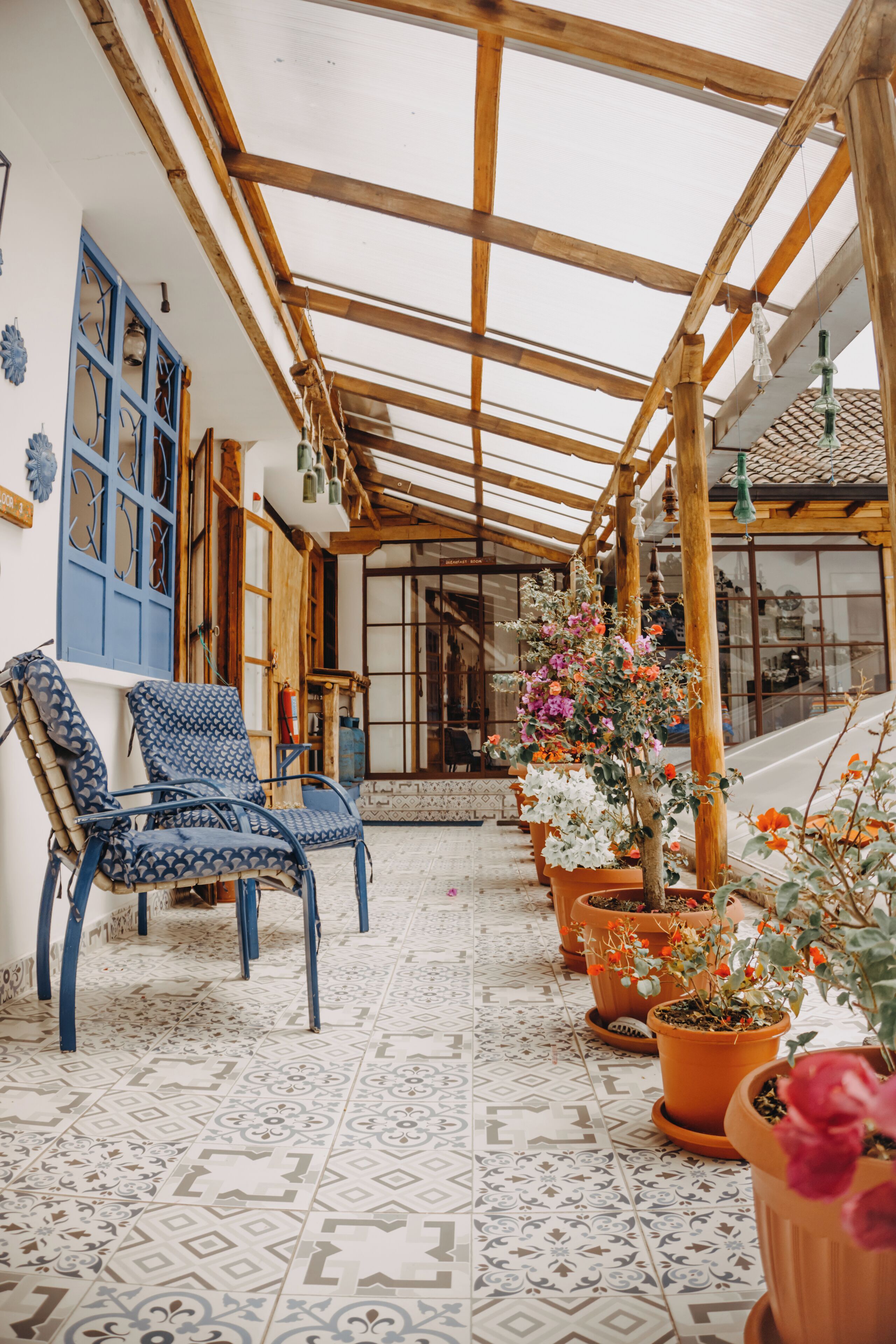 Un patio techado con vigas de madera, baldosas de suelo estampadas y macetas con plantas.