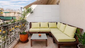 A balcony with a wooden sectional sofa, a small table, and potted plants. - AthenSunapartment  Top floor / 5" metro (Athina)