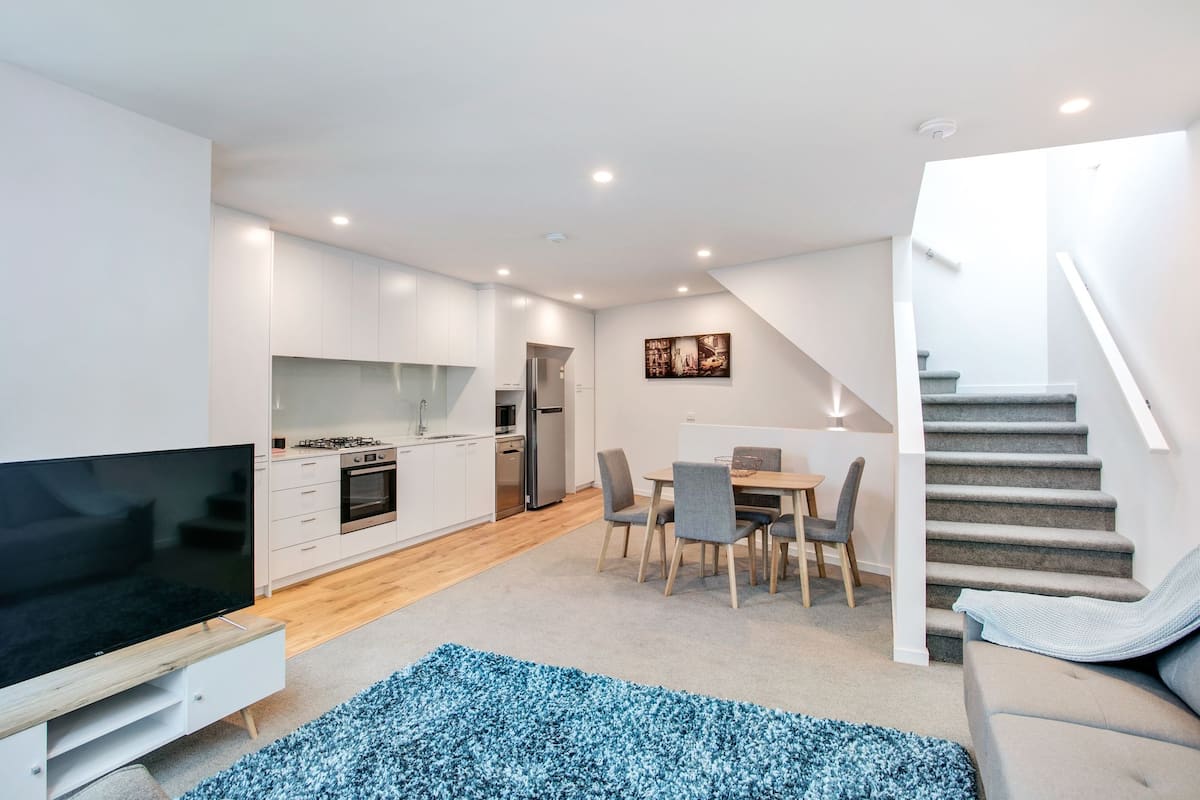 A modern apartment with a kitchen, dining area, and a staircase leading to an upper level.