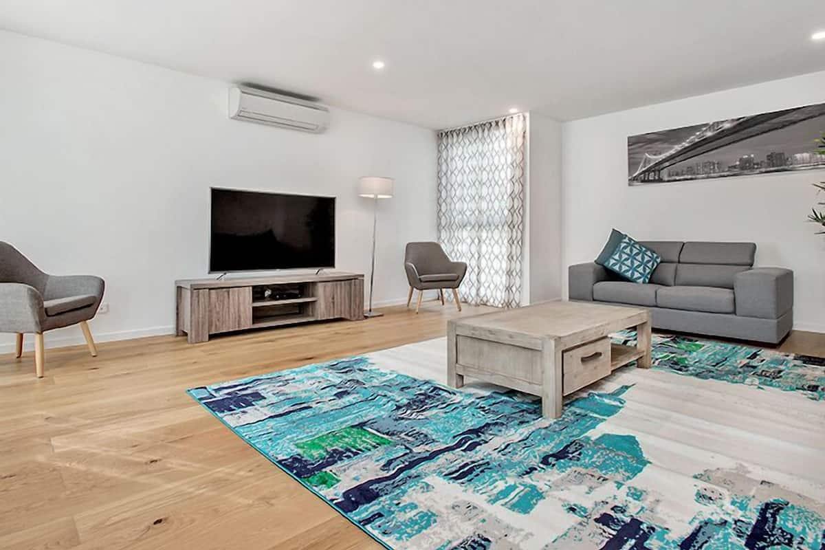 A modern living room with a flat-screen TV, grey sofa, and a patterned rug.