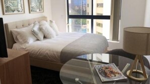 Ein Hotelzimmer mit einem Bett, einem Glastisch mit einer Zeitschrift und einem Fenster mit Blick auf die Stadt.