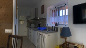 Ett kompakt kök med mikrovågsugn, brödrost och kaffebryggare. Det finns ett fönster med gardiner, en diskho och ett litet bord med en lampa.