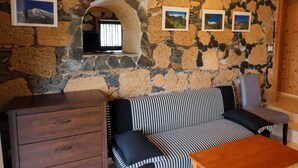 Une pièce aux murs de pierre, avec un canapé, une table en bois et un téléviseur fixé au mur.