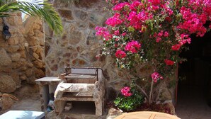 Un mur de pierre avec un barbecue et une table dans un espace extérieur ensoleillé.