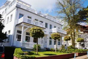 Ein weißes Gebäude mit Balkonen und einem Garten davor.