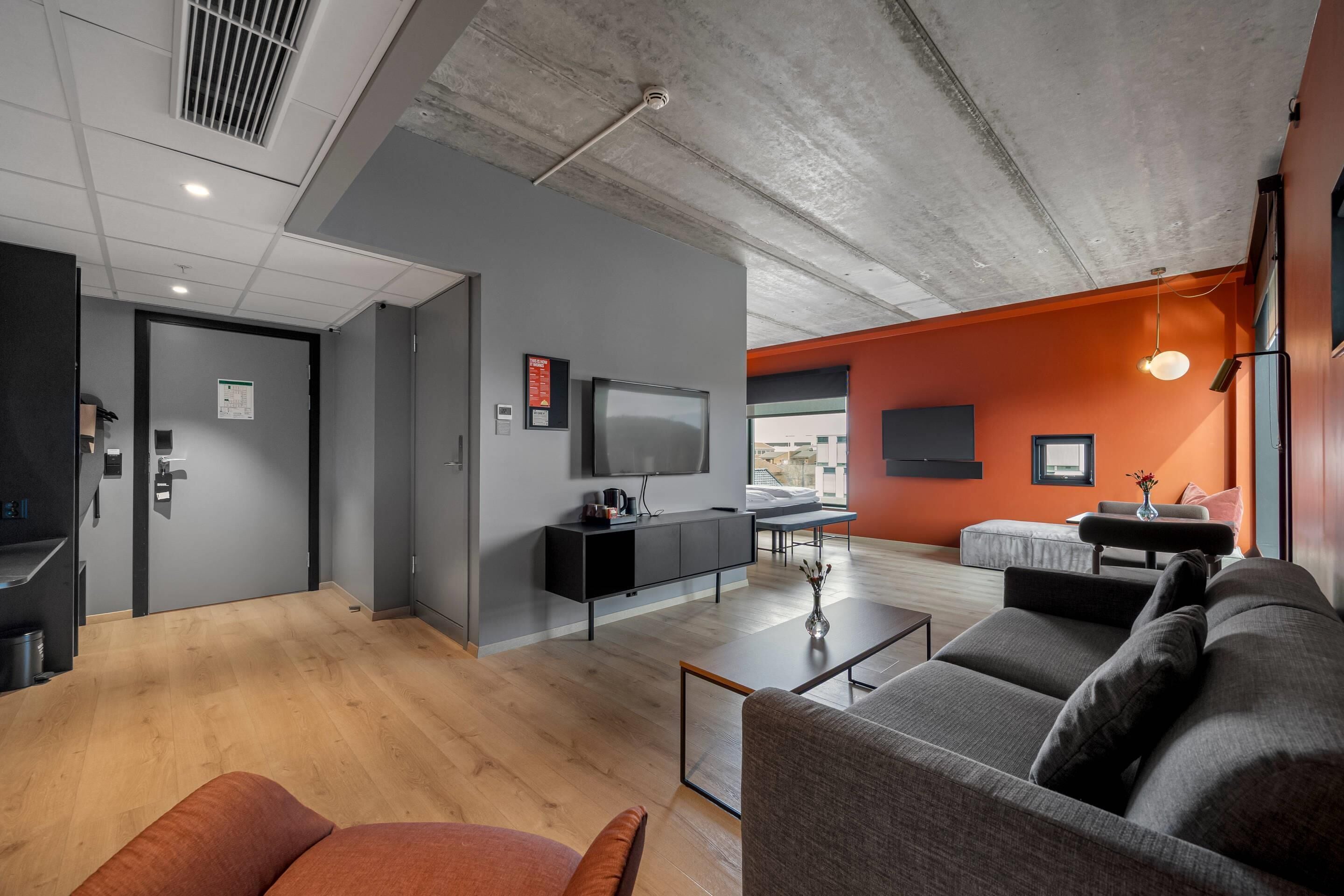 Een moderne woonkamer met een grijze bank, een salontafel en een aan de muur bevestigde televisie.