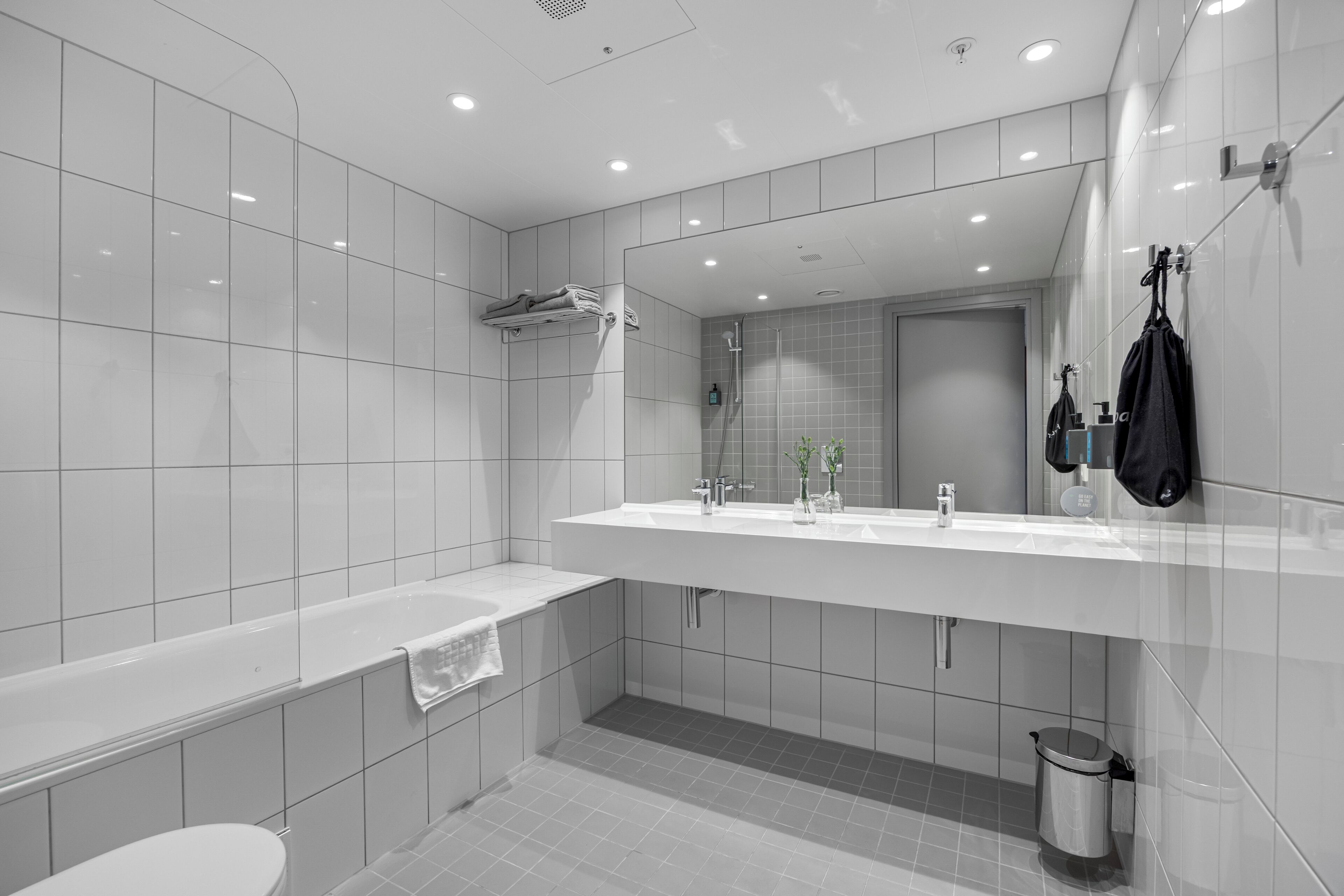 A modern bathroom with a large mirror, two sinks, a bathtub, and a shower.