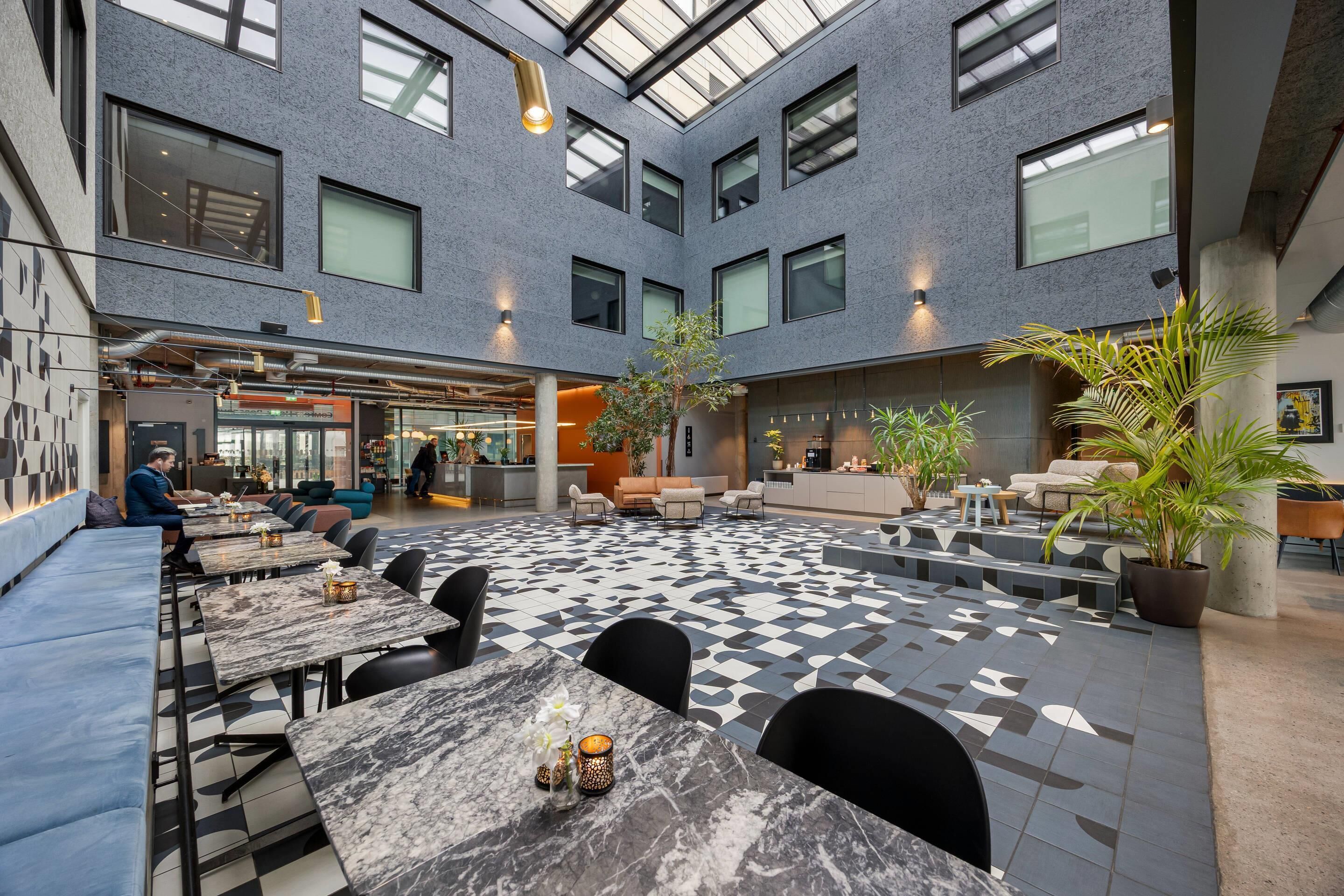 A modern interior with a checkered floor, seating areas, and a high ceiling with skylights.