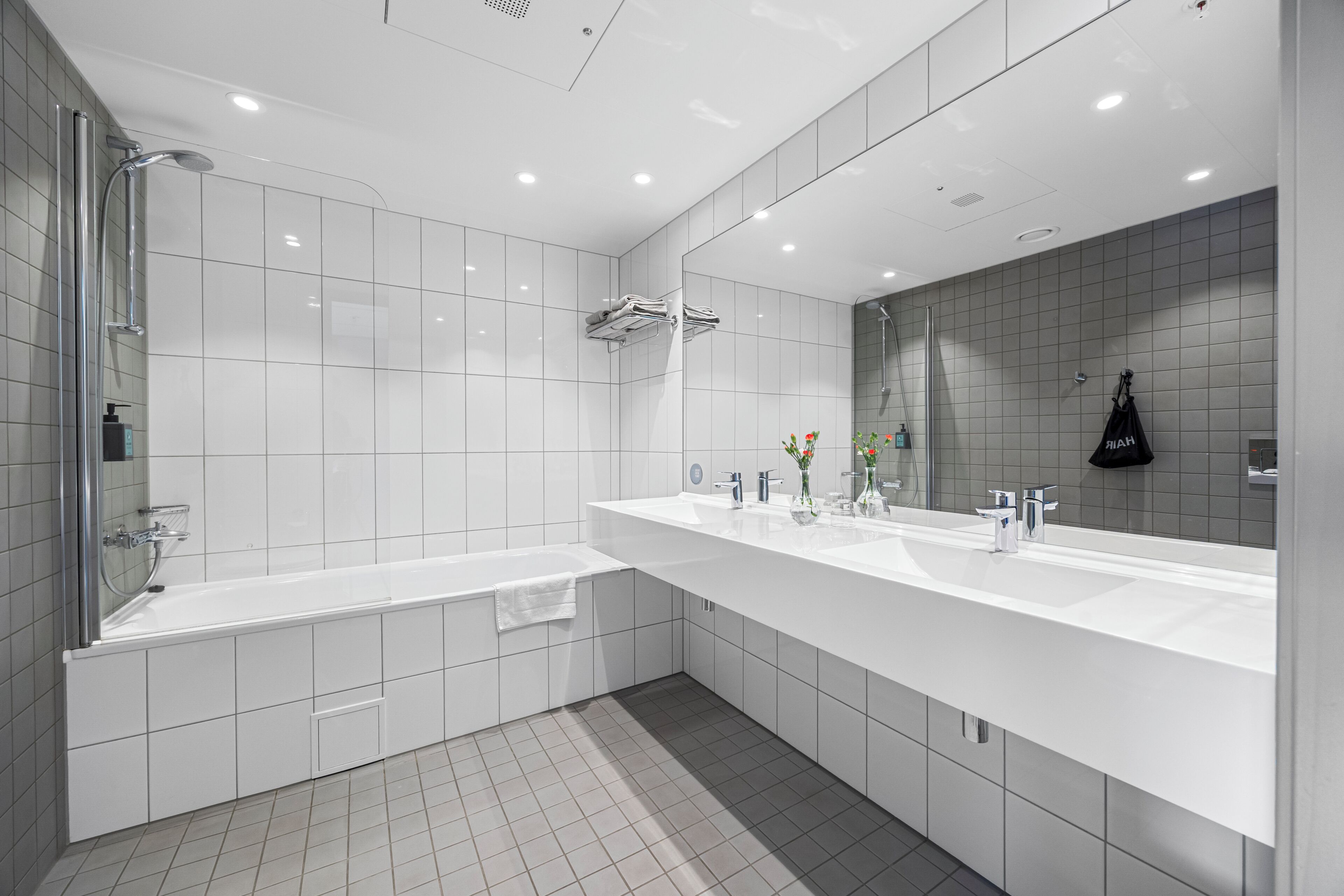 Un baño moderno con un espejo grande, dos lavamanos, una bañera y una ducha.