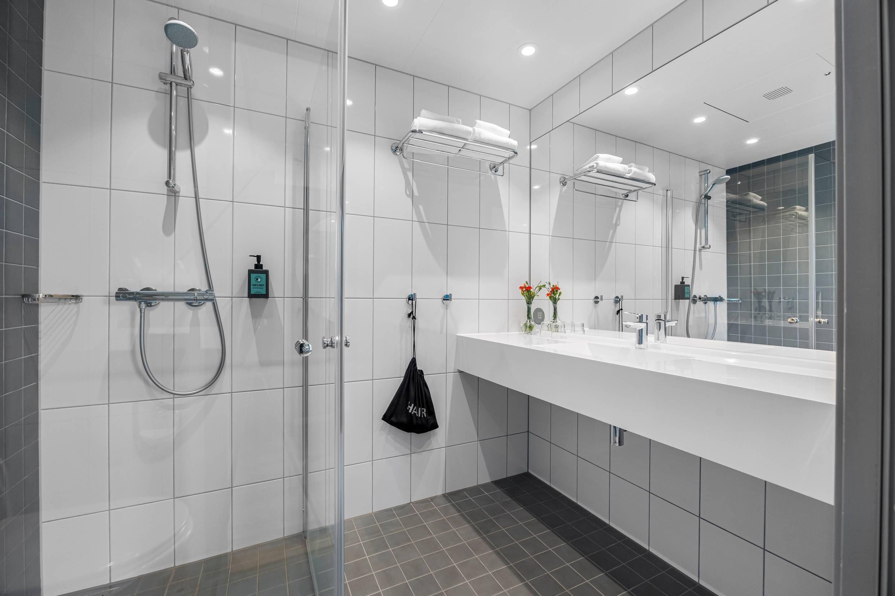 A modern bathroom with a glass shower enclosure, a white vanity with a mirror, and a black bag hanging on the wall.