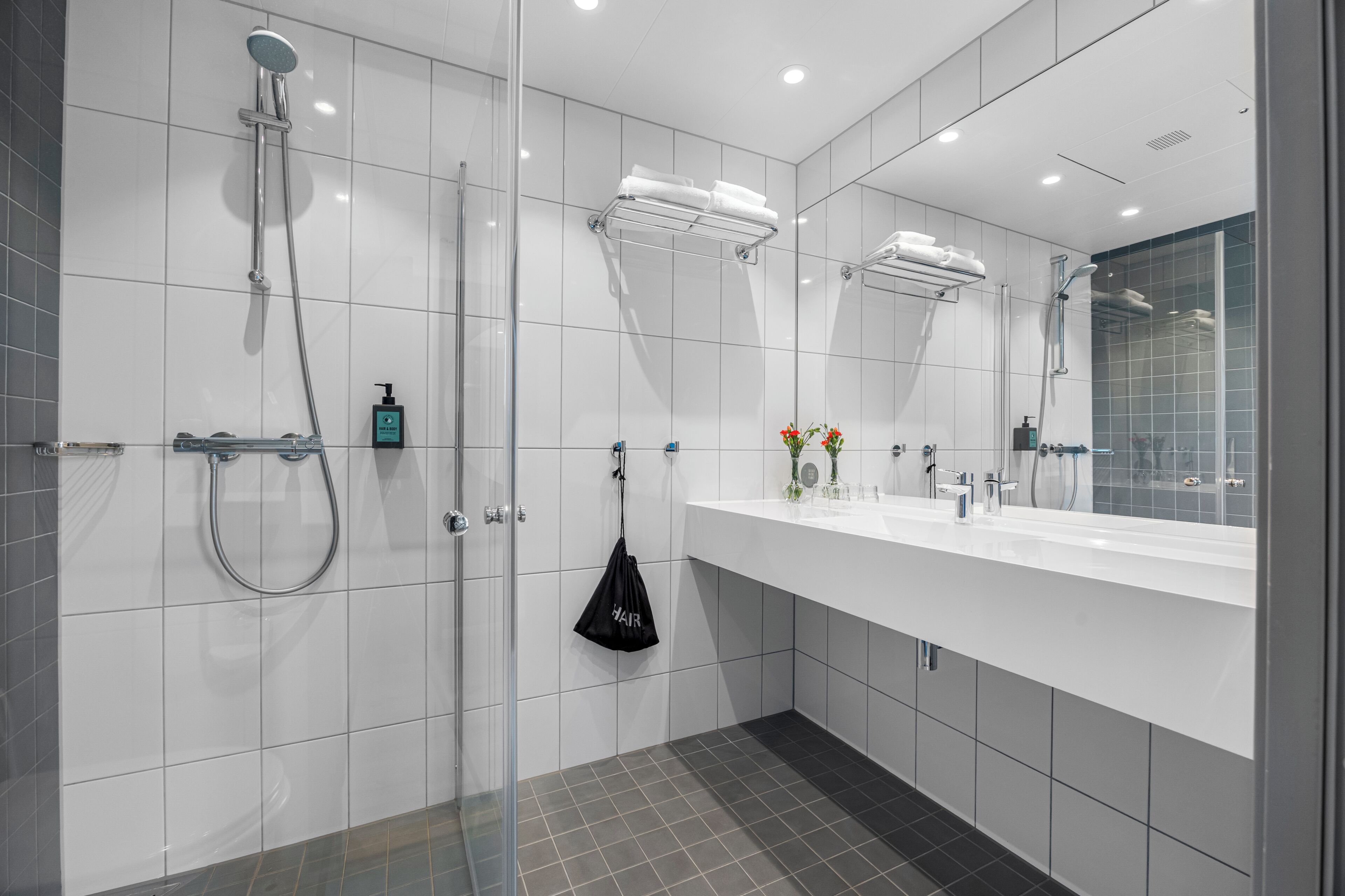 A modern bathroom with a glass shower enclosure, a white vanity with a mirror, and a towel rack.