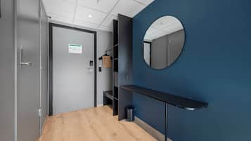 Un pasillo con suelo de madera, pared azul, espejo redondo, estante negro y una puerta con un letrero.