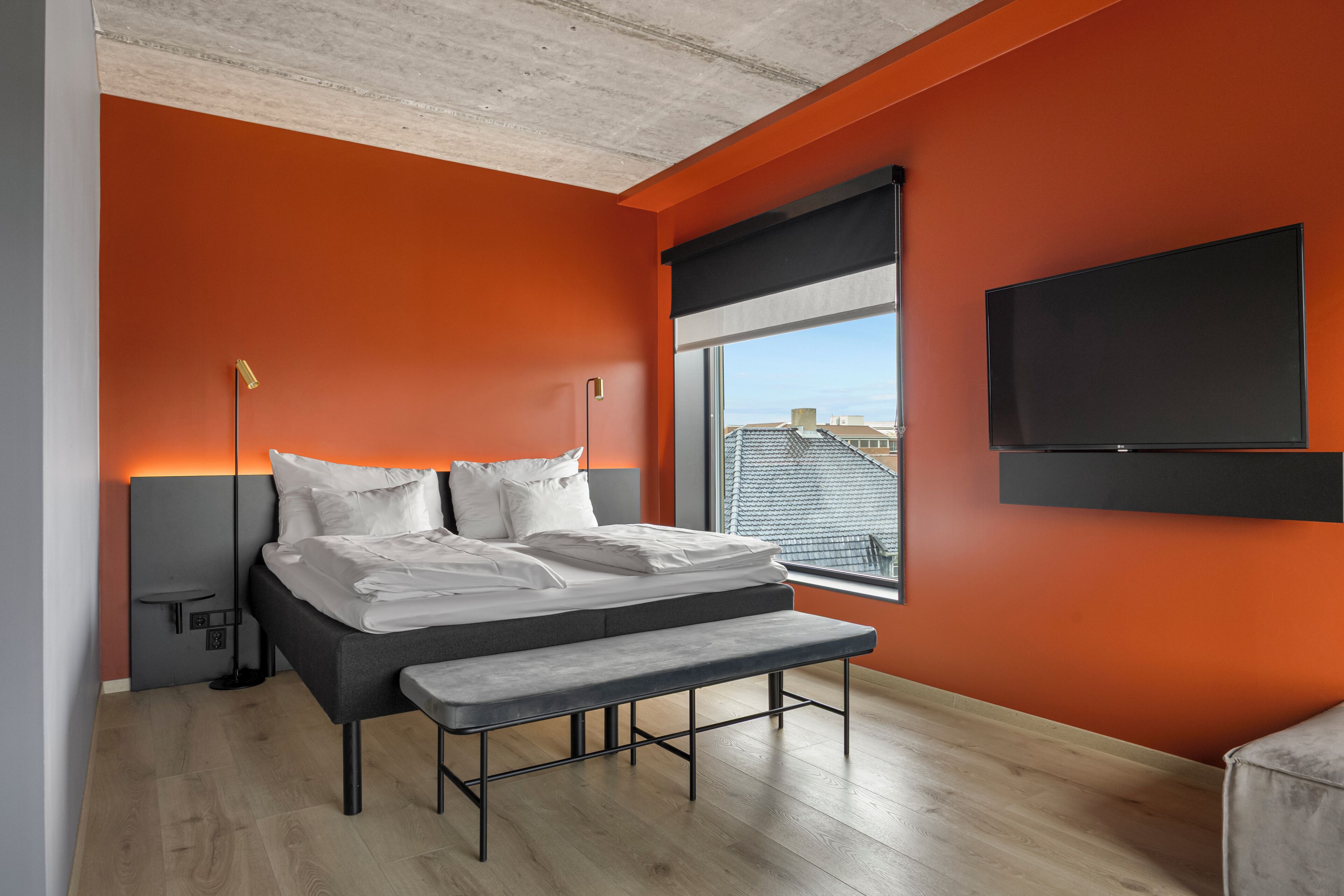 A modern bedroom with a bed, bench, bedside table, and a TV mounted on the wall.