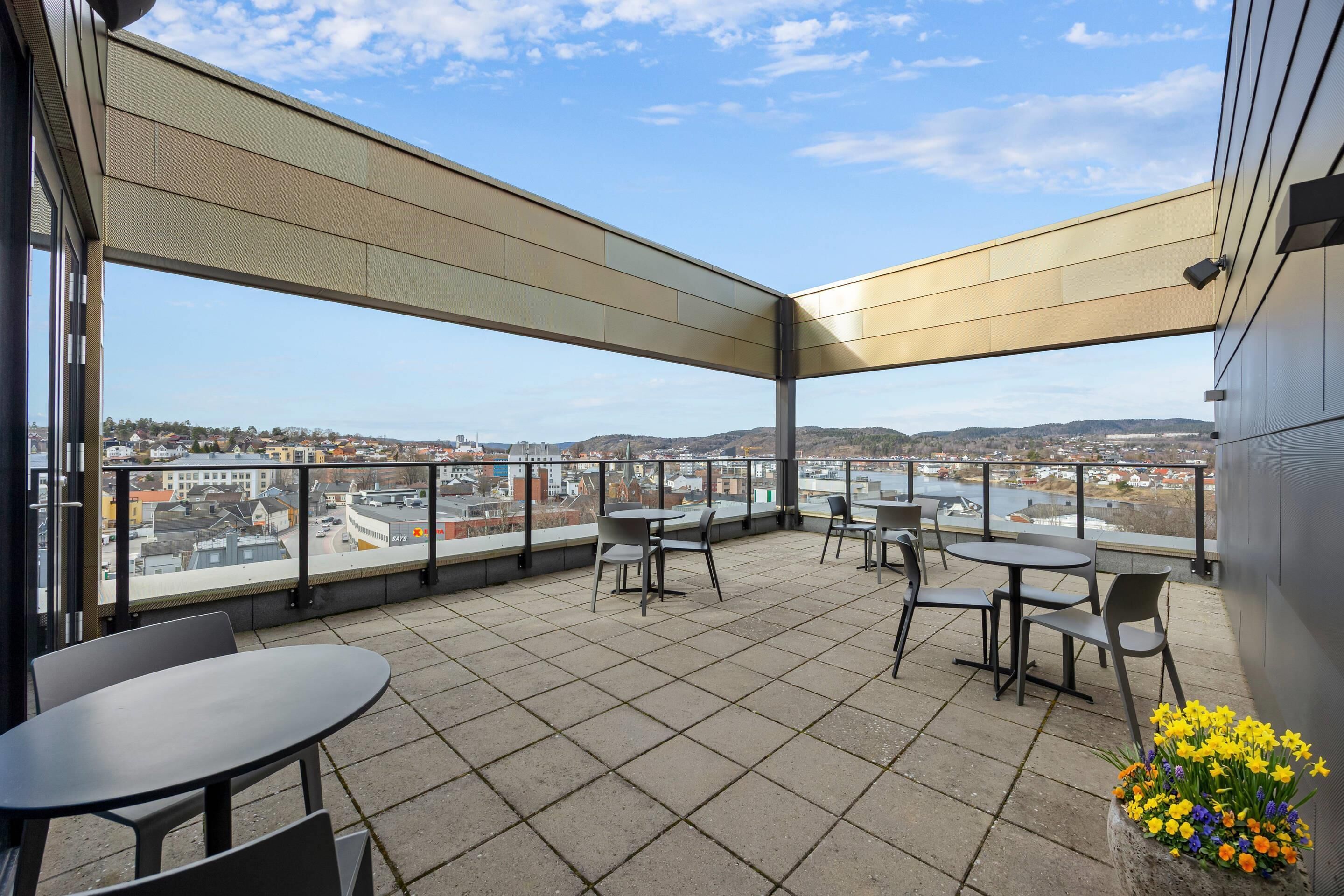 A terrace with tables and chairs, a view of the city, and a flower arrangement.