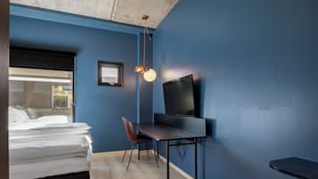 Une chambre avec un lit, un bureau et une chaise, une télévision et une fenêtre avec des stores.
