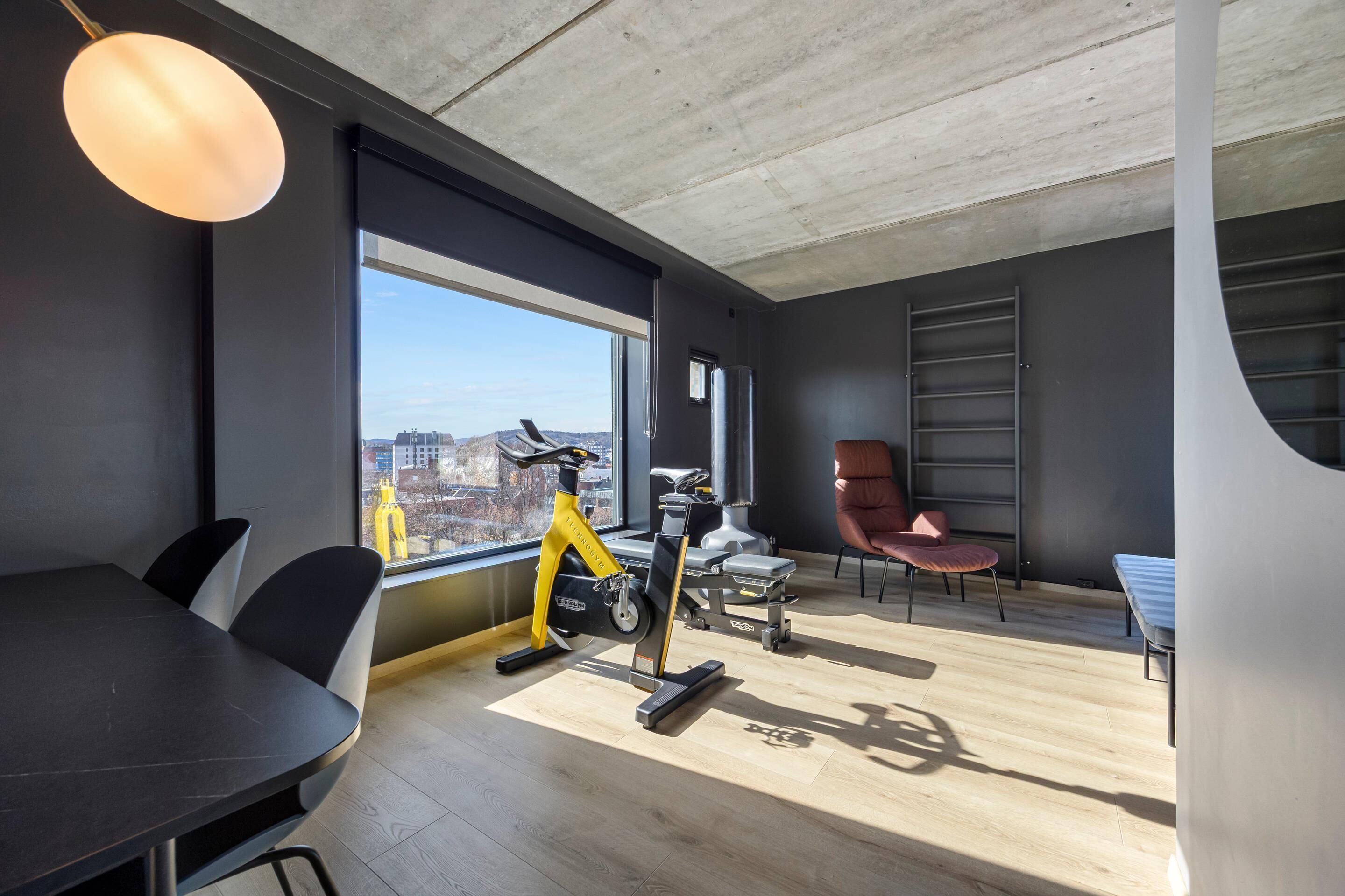 Een moderne kamer met een groot raam, een hometrainer, een massagetafel en een eettafel.